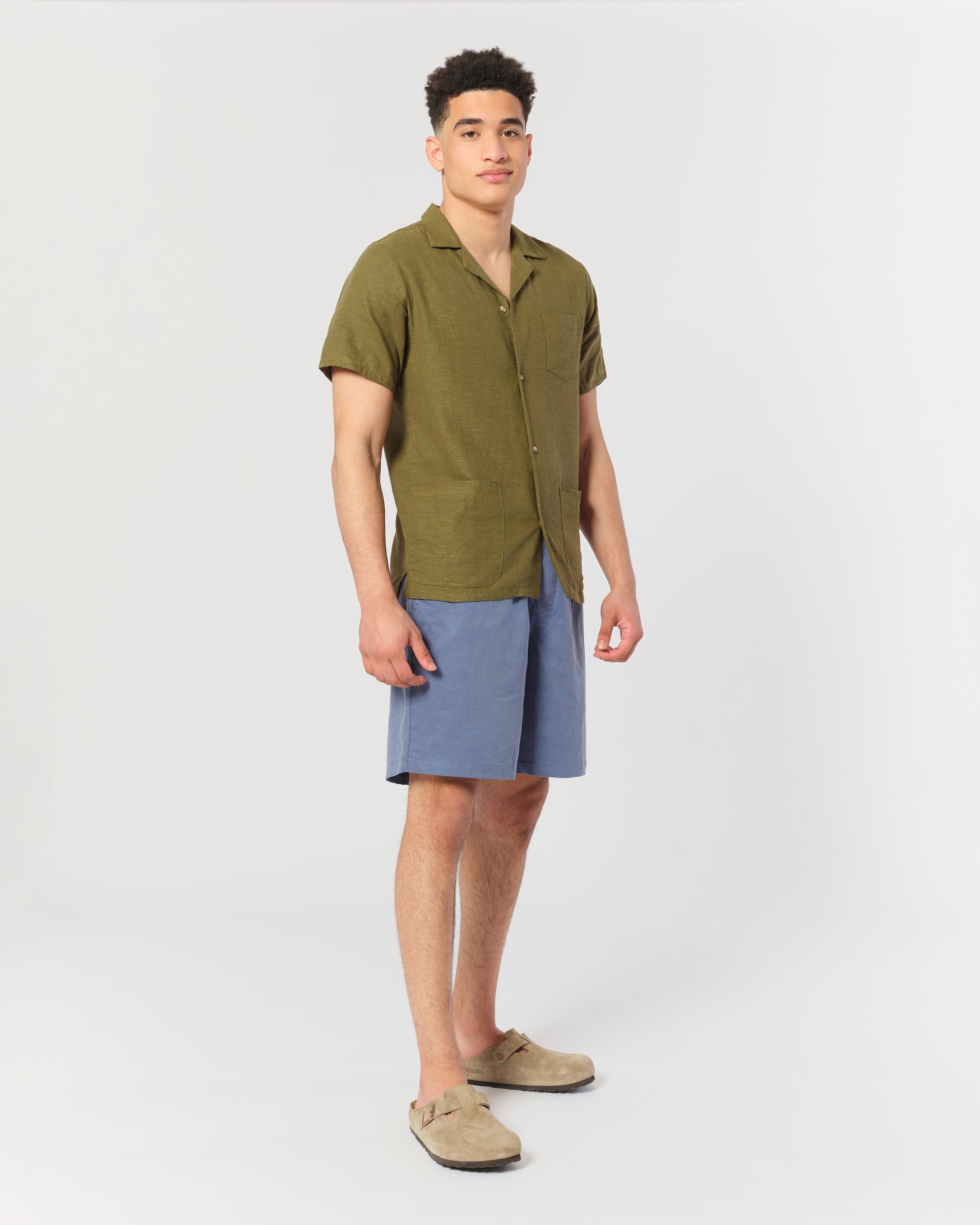 An olive green linen camp shirt with a chest pocket and two lower pockets on the front shot on model
