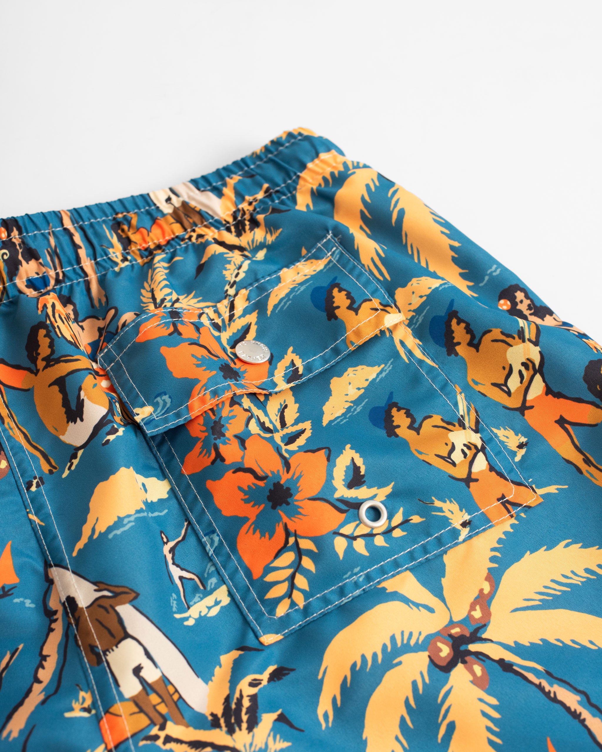 Close up of back pocket on blue swim trunk with Hawaiian-inspired printed beach scene