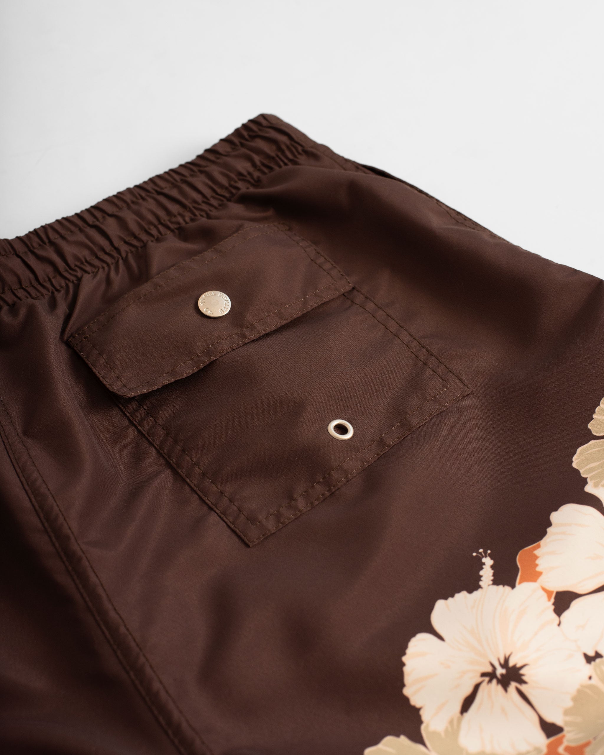 Close up back pocket shot of Brown swim trunk with floral print on the bottom of the leg