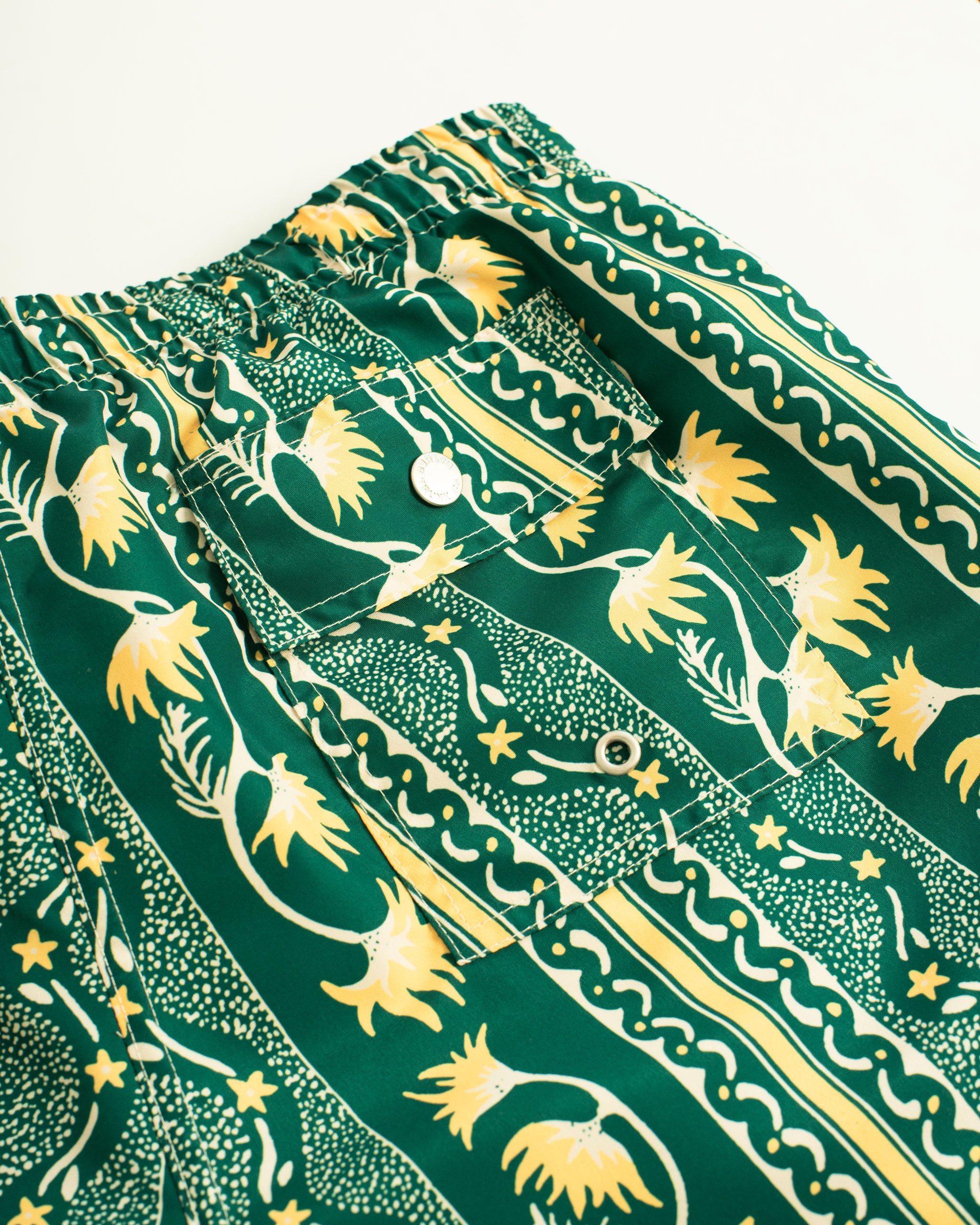 shot of back pocket of green swim trunk with yellow and white classic stripe features intricate mosaics of flowers, sand, and starfish