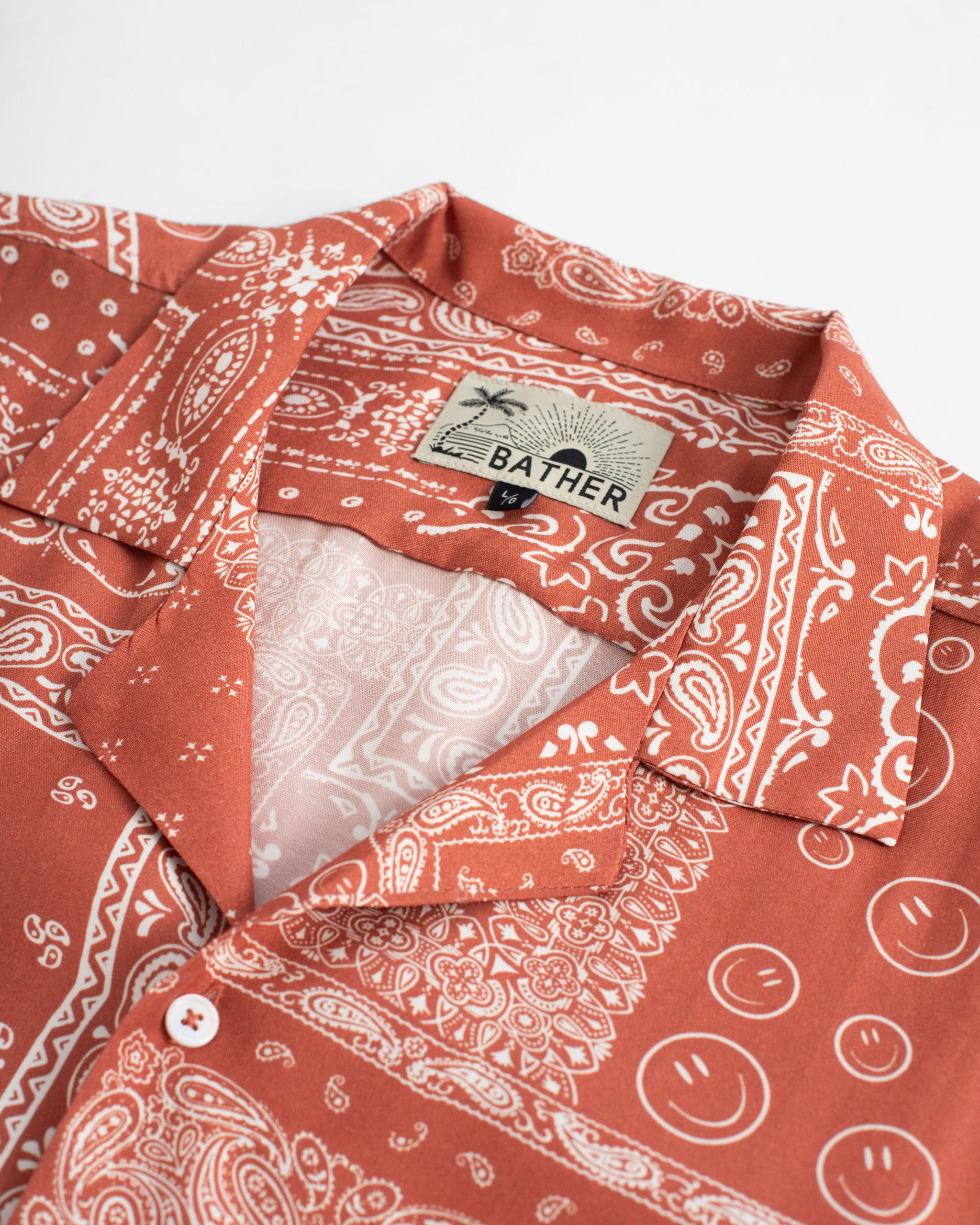 Collar close up of A terracotta red camp shirt with an all-over bandana print