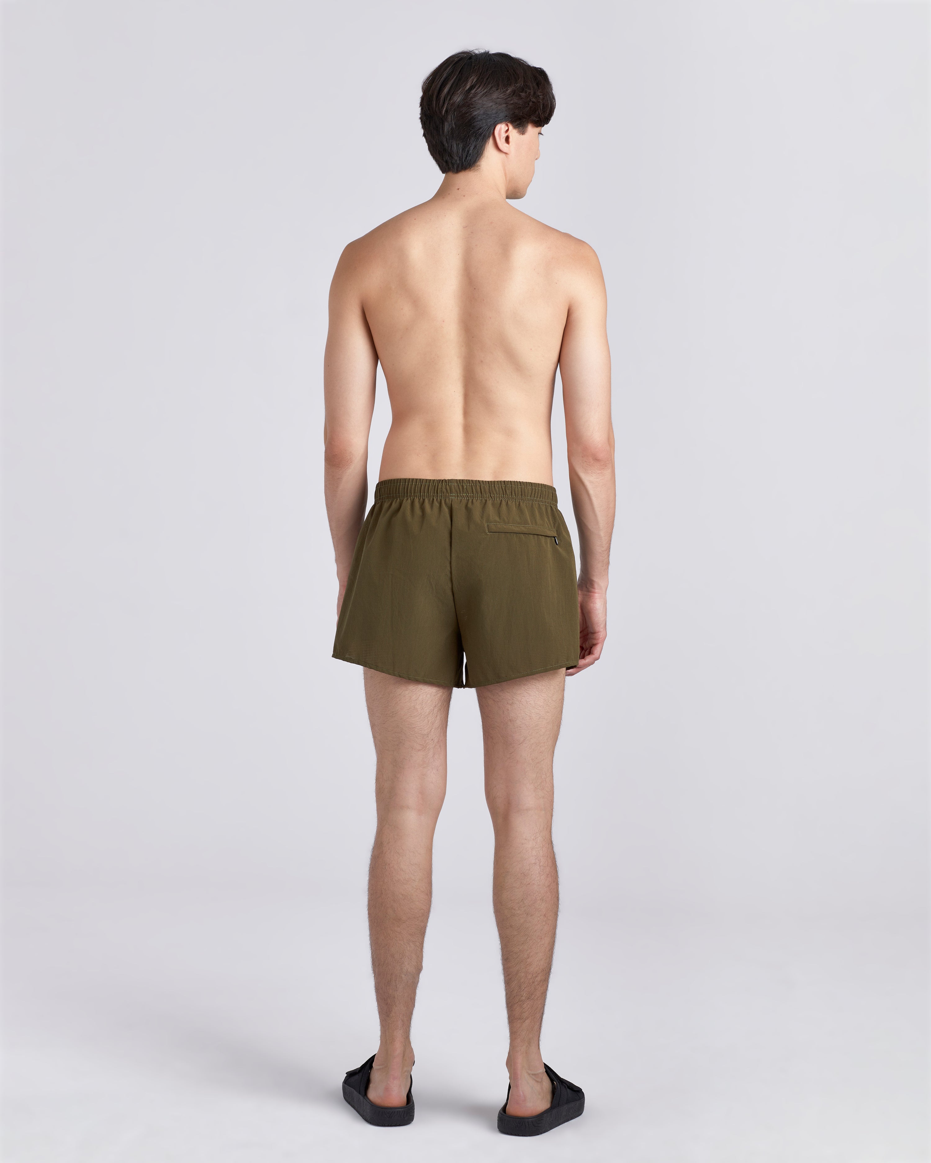 Back view of shirtless model wearing sandals and 3.5 inch inseam Bather Active Trunk in green featuring lightweight recycled Japanese DotAir nylon with stretch fabric and compression liner