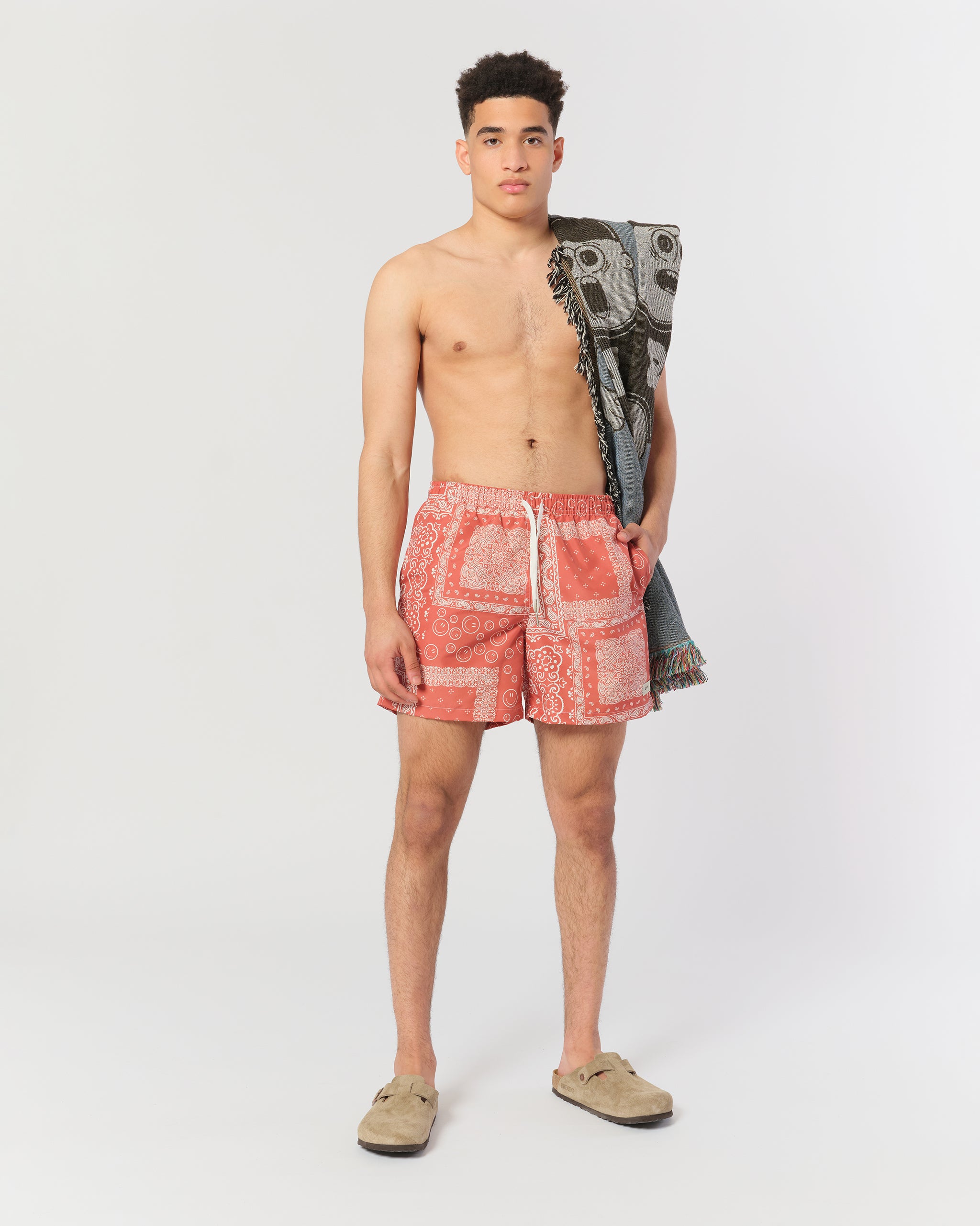 A terracotta red swim trunk with an all-over bandana print shot on model