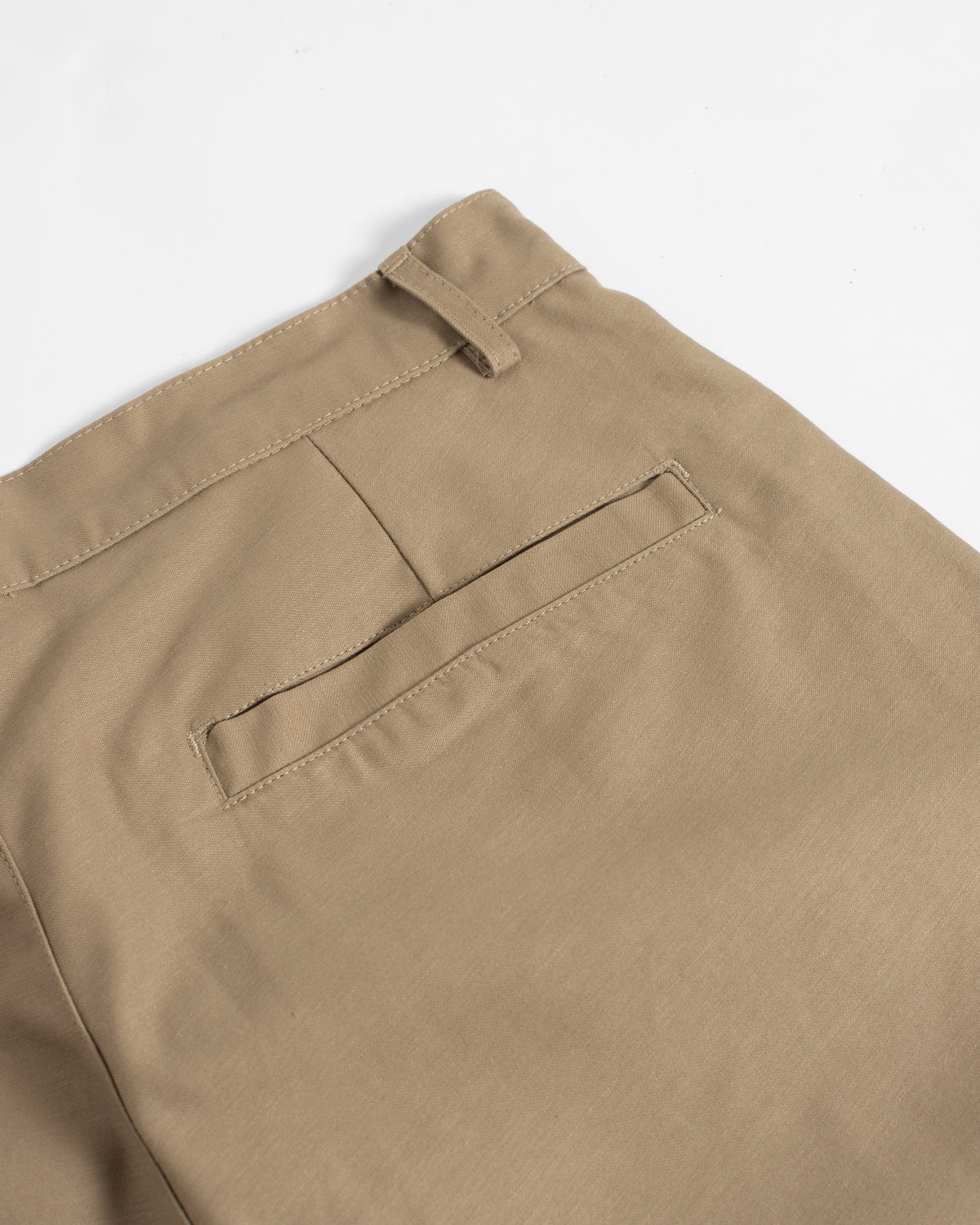 Close-up of khaki trousers showing the waistband, belt loop, and a side welt pocket on a clean white background.