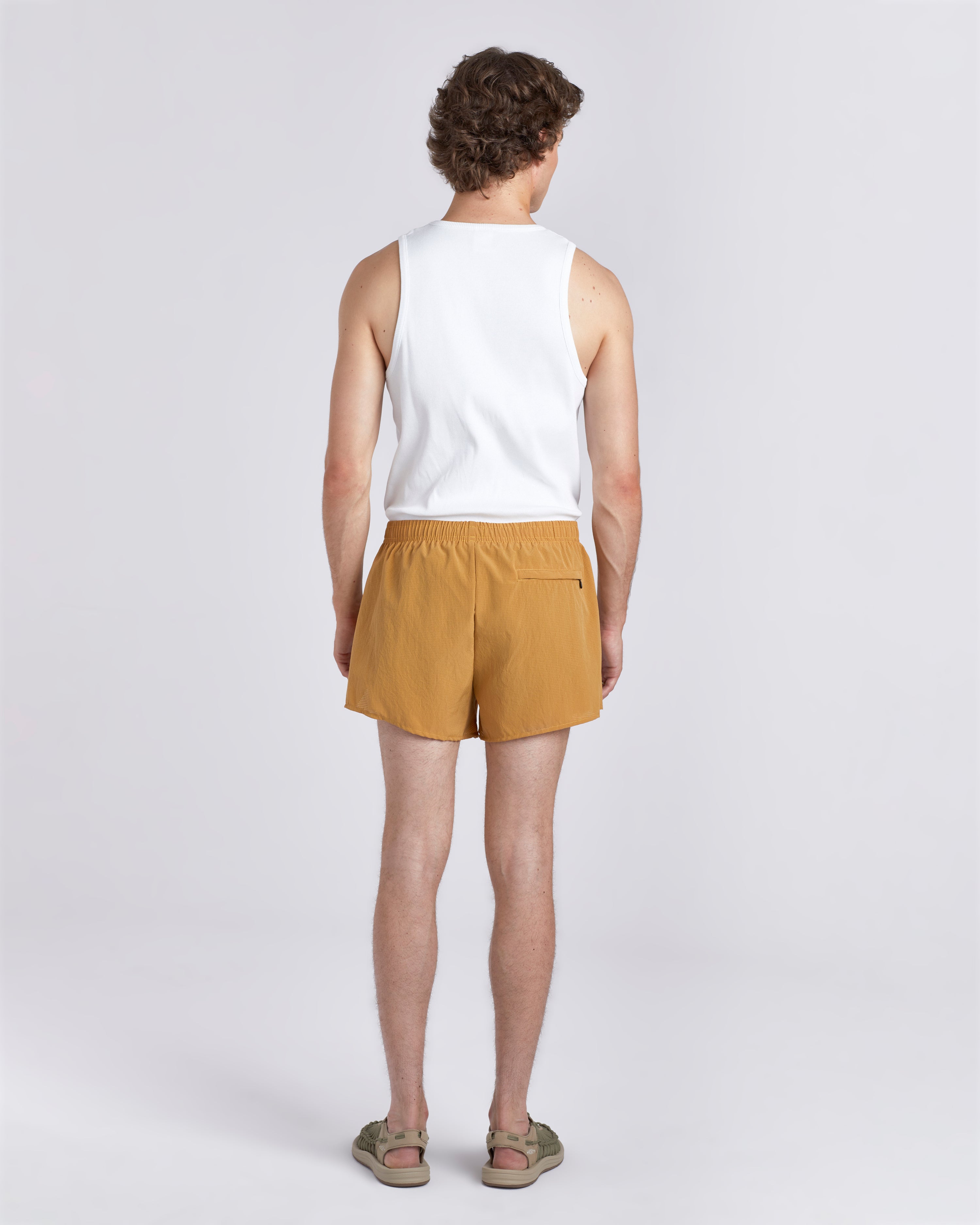 Back view of model wearing white tank top and 3.5 inch inseam Bather Active Trunk in yellow featuring lightweight recycled Japanese DotAir nylon with stretch fabric and compression liner
