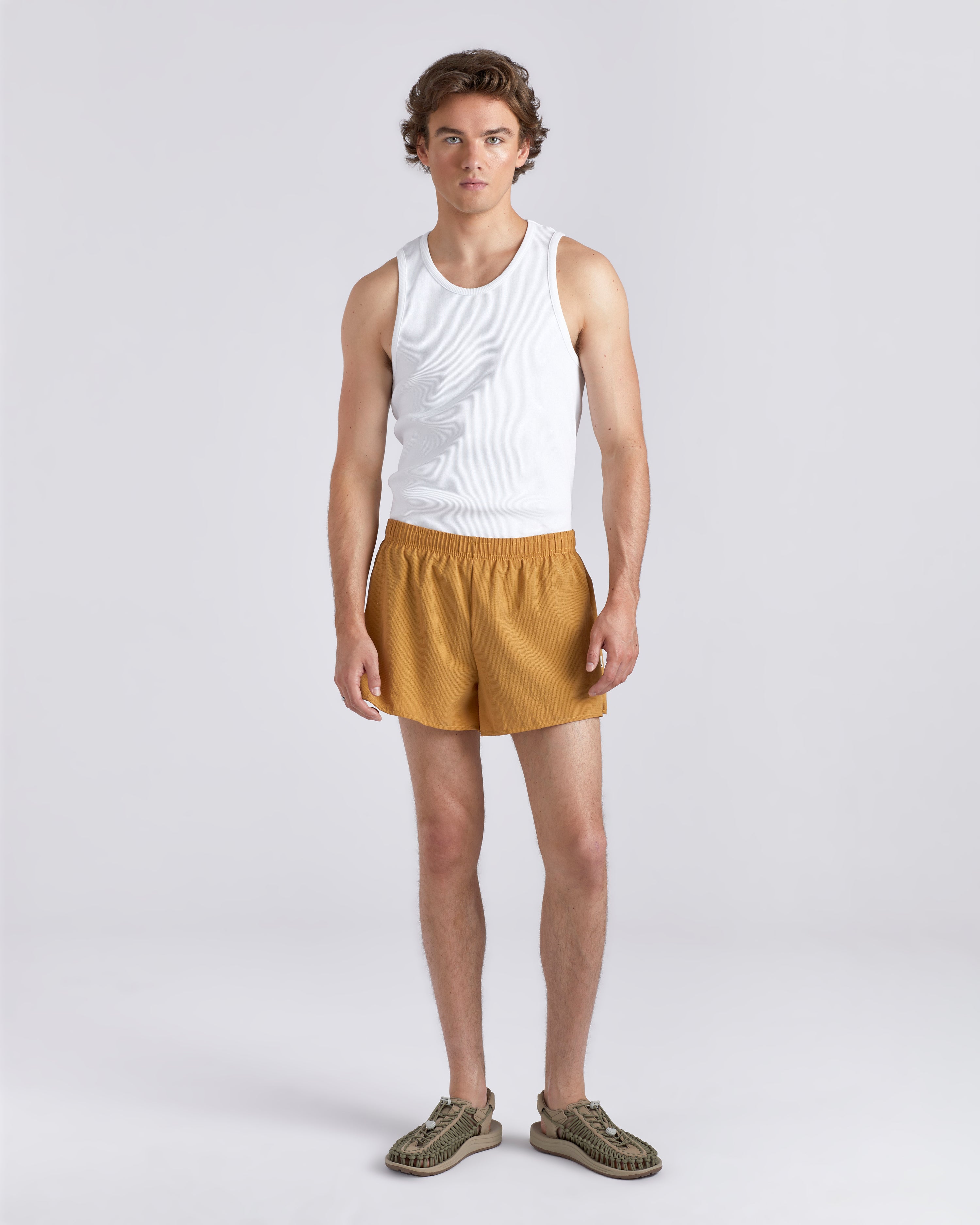 Front view of model wearing white tank top and 3.5 inch inseam Bather Active Trunk in yellow featuring lightweight recycled Japanese DotAir nylon with stretch fabric and compression liner