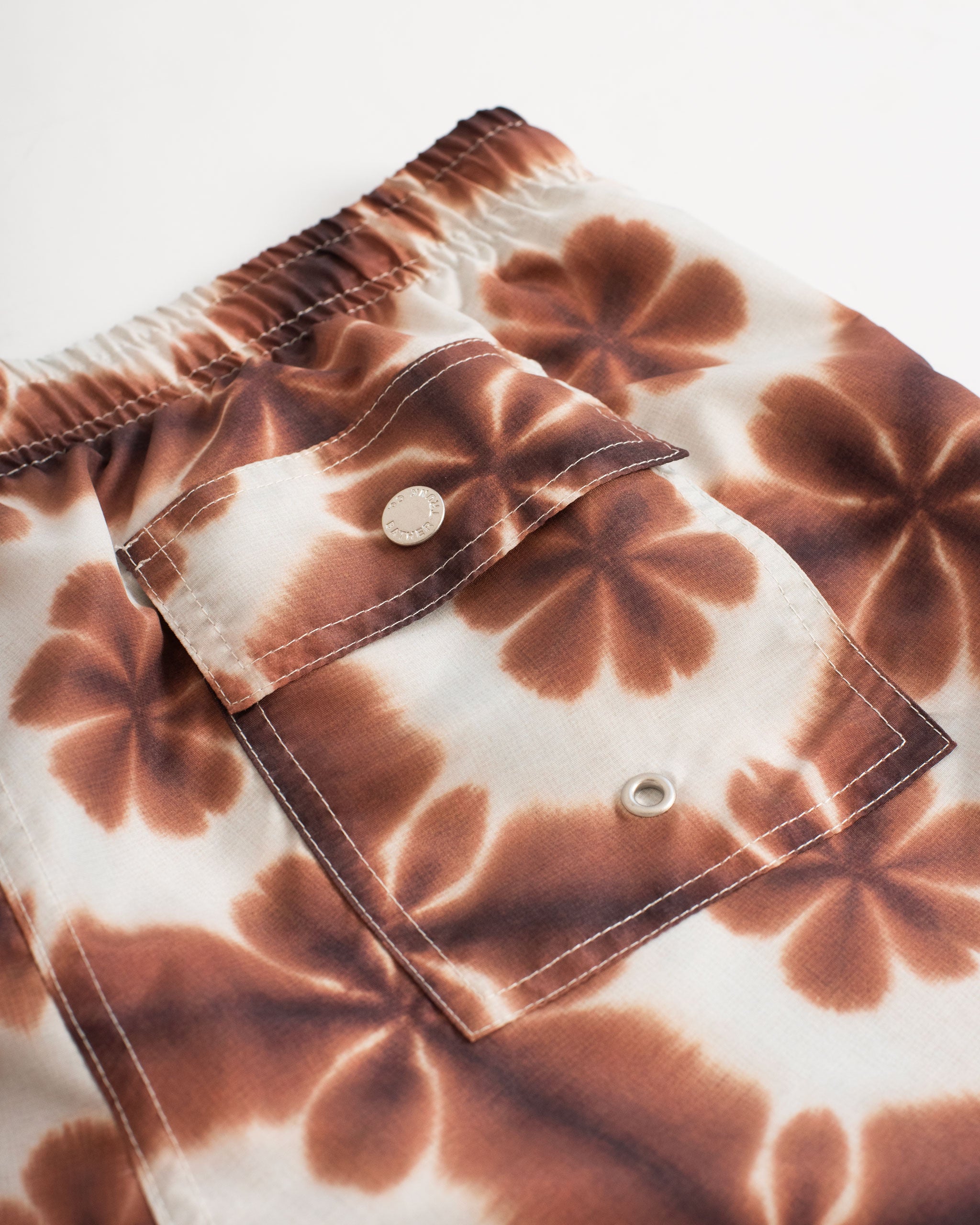 Back pocket close up shot of Brown swim trunk with a shibori-inspired print that looks like a kaleidoscope pattern