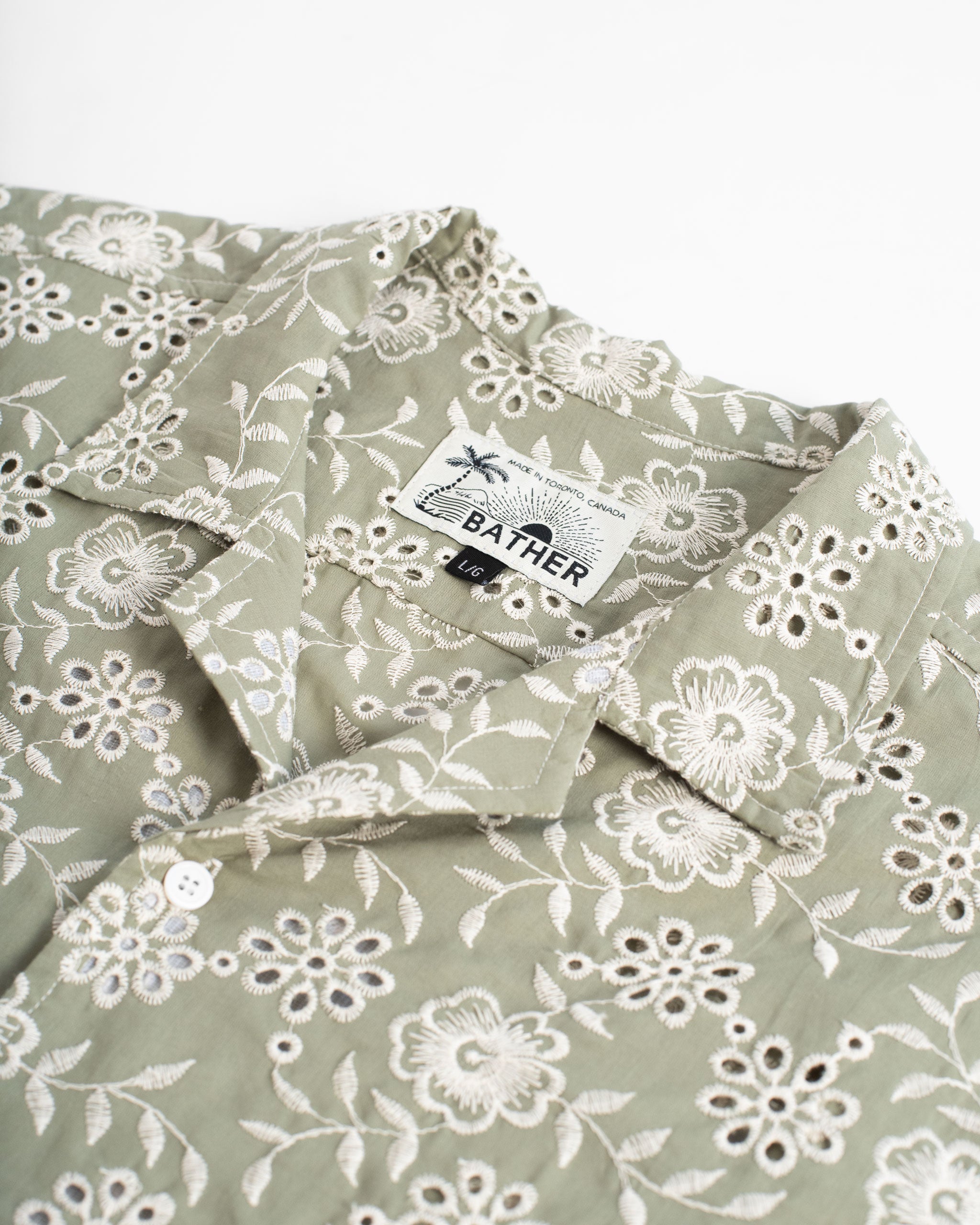 Collar close up of A sage green camp shirt with an all-over embroidered floral pattern