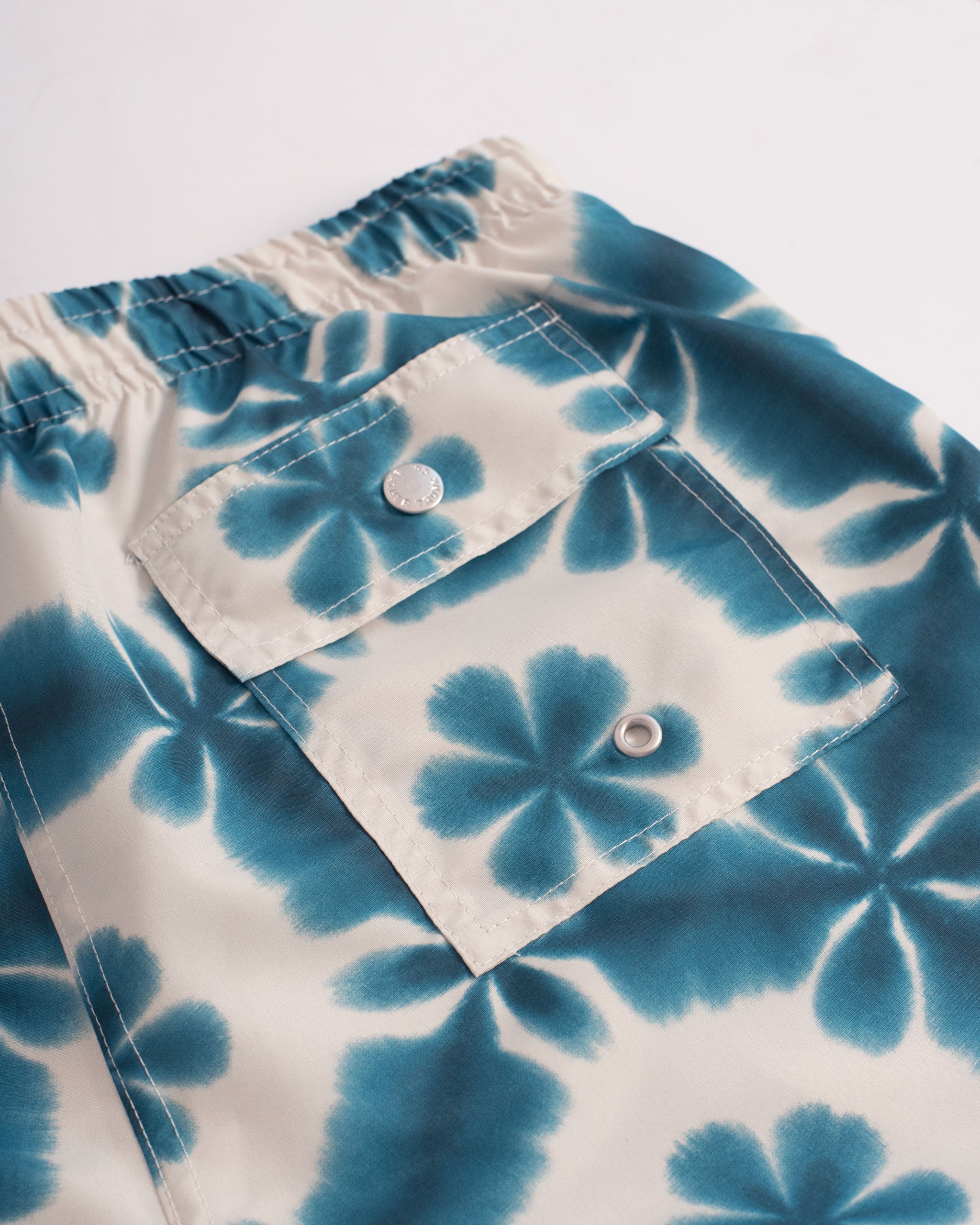Back Pocket Shot of A blue swim trunk with a shibori inspired pattern, similar to a kaleidoscope